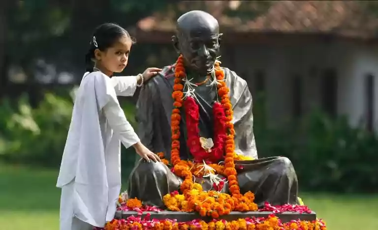 Girl in Whilte dress poses next to a statue of Gandhi Ji
